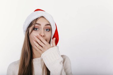 Avrupa kadın ağzını el ile kapsayan santa şapkalı. Kız bir şey tarafından şaşırttı. Genç ve güzel model sarı uzun saçlı, geniş kaşları ve mavi gözlü Studio fotoğraf makinesinde poz ile. izole.