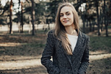 Uzun sarı saçlı genç kadın kameraya bakarak ve gülümseyen pardesü giymiş. Sonbahar. Açık. Orta atış