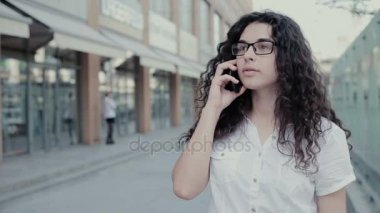 Genç kadın cep telefonda konuşurken. Kötü gününde diyorsun telefonda kızla. Uzun kıvırcık saçları beyaz gömlek, siyah etek ve gözlük giymiş olan model. Kopya alanı.