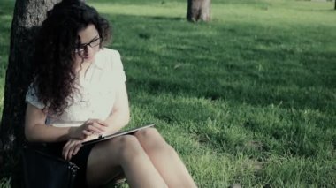 Çimenlerin üzerine oturmuş ve tablet bilgisayarını kullanarak genç karışık ırk kadın