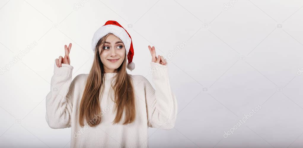 Happy young woman with blond hair and in santa hat crossed her fingers 