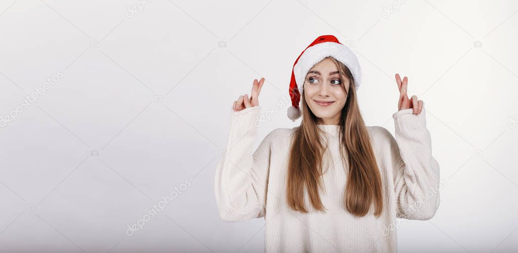 The happy girl in santa hat cross fingers in hope