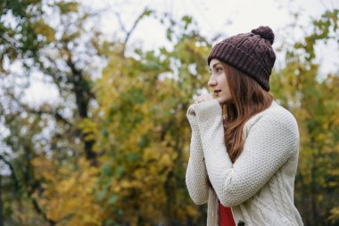 Birlikte katlanmış kız ve sıcak elleri çalışın. Sıcak kış şapka ve kırmızı fular modeli. Sonbahar Park yaprakları arka plan üzerinde duran kadın. Açık. Soğuk. Sonbahar.