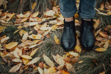 Kadın leags duran sarı yapraklar ile ıslak sonbahar yere. Siyah deri çizme ve kot giyen kadın. Sonbahar. Açık.