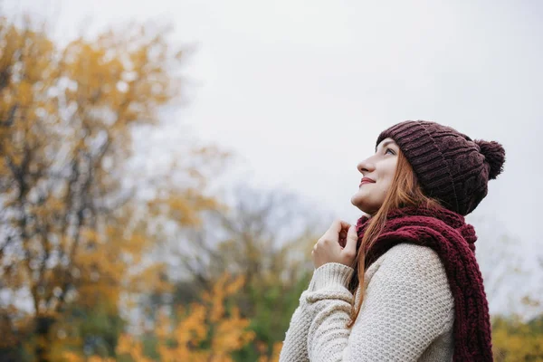 Sıcak kış şapka, kazak ve kırmızı eşarp ve gökyüzü üzerinde ararken model. Kız kollarını birlikte göğüs üzerinde katlanmış. Eşarp üzerinde ellerini tutan kadın. Açık. Profil portre.