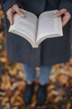 Erkek açık kitap tutan eller. Kadın açık kitap okuyun. Gri ceket mavi kot pantolon ve siyah çizmeler giyen model. 