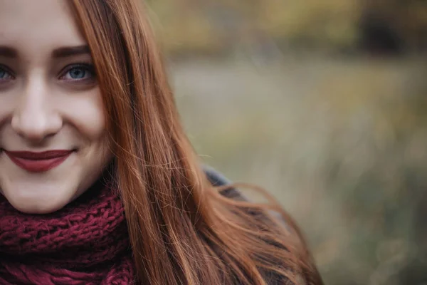 Woman with romantic face and full lips looking at camera and smiling. Portrait of beauty woman with red hair and green eyes. The girl wearing grey wool coat and red scarf. Portrait with half face.