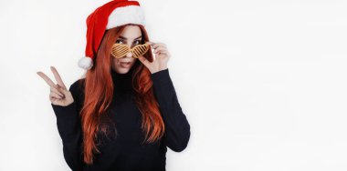 Komik ve eğlenceli genç readhead kadın Sunta Claus şapka ve wink kameraya veren ve barış sembolü yapma eller tarafından tasarlanmış gözlük