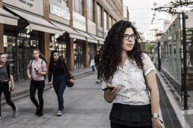 Genç ve şehir arka plan üzerinde duran güzel karışık ırk kadın. Sokakta duran ve yan bakarak kadın. Cep telefonu elinde tutan genç bayan