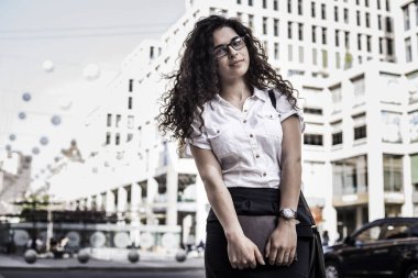 Genç ve güzel kadın şehir arka plan üzerinde duruyor. Sokakta duran ve kamera ve gülümseme bakarak Amerikan karışık ırk kadın. Elinde defter tutan genç bayan