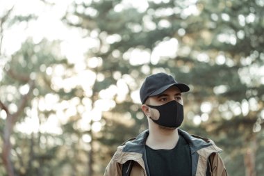 Ağaçların arkasında tıbbi maskeli bir adamın portresi.