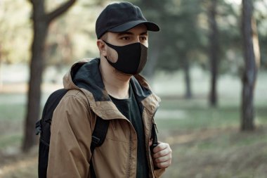 Tıbbi maskeli bir adam insanlardan uzakta parkta yürüyor. Adam temiz hava soluyor.