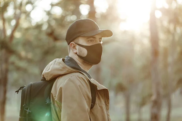 Tıbbi maskeli kendine güvenen bir adam sırt çantasıyla parkta yürüyor.