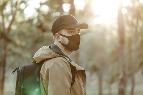 уверенный в себе человек в медицинской маске ходит по парку с рюкзаком
