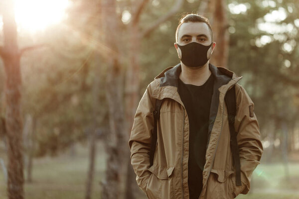 Портрет человека в медицинской маске. Взрослый человек в черной маске стоит в парке и смотрит в сторону
