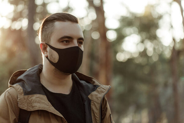 Закрыть портрет человека в медицинской маске. Молодой человек стоит на фоне деревьев и смотрит в камеру. На улице. Здравоохранение и уход. Вирус
