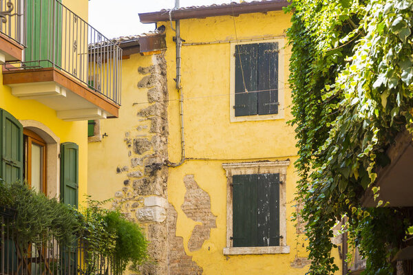 Old yellow house facade, green window shutters and balcony in popular touristic village Garda, Italy