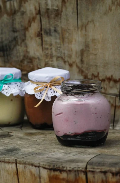 Makanan penutup krem dalam toples kaca kecil dengan pita pada latar belakang kayu — Stok Foto