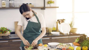 Asyalı kadın salata yapıyor ve telefonda ciddi bir yüzle konuşuyor..