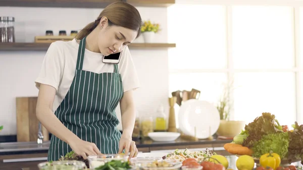 Asyalı kadın salata yapıyor ve telefonda konuşuyor..