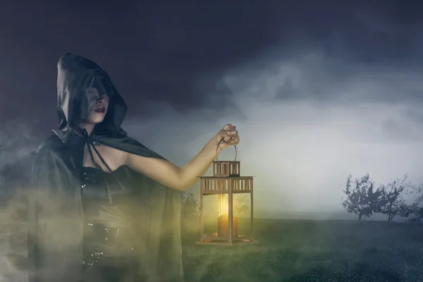 Beautiful asian witch girl holding a lantern with a cloak on his head — Stock Photo, Image