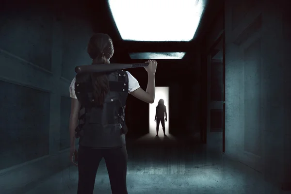 Молодая женщина держит бейсбольную биту, стоящую в темном коридоре с зомби — стоковое фото
