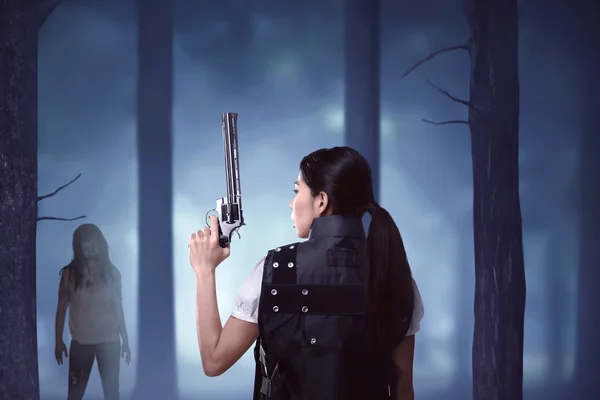 Griezelige zombie kijken naar Aziatische vrouw met pistool — Stockfoto