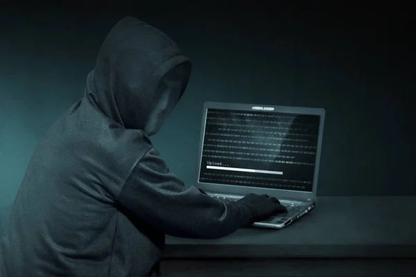 连帽的黑客在掩码中使用的便携式计算机 — 图库照片