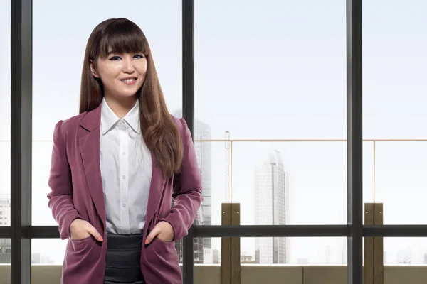Улыбающаяся азиатская деловая женщина, стоящая перед окнами — стоковое фото