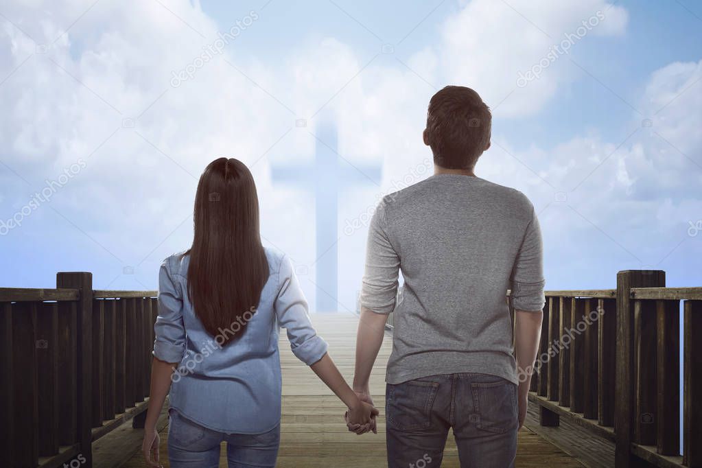 Asian couple looking at bright cross sign