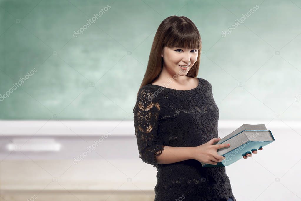 Pretty asian teacher holding books on class