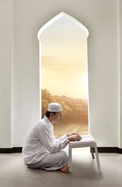 Genç Asyalı Müslüman adam kutsal kitabı Kur'an okurken kapaklı