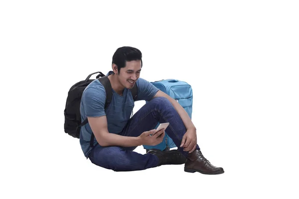 Портрет молодого человека, сидящего с чемоданом и отправляющего текстовое сообщение — стоковое фото