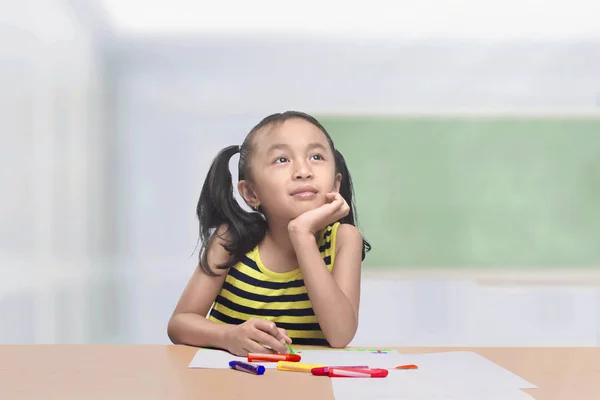 Забавная азиатская девочка с цветными карандашами думает: — стоковое фото