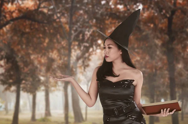 Красивая азиатка в ведьмовском платье с открытой книгой о ладони — стоковое фото