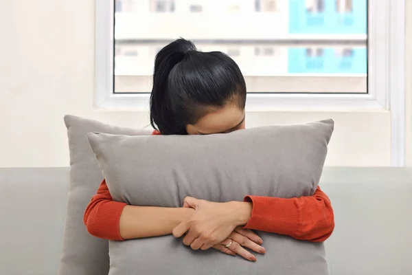 Junge asiatische Frau umarmt und versteckt sich hinter einem Kissen — Stockfoto