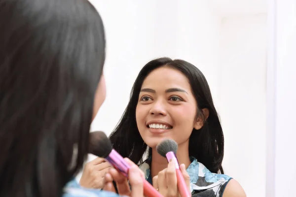 Hermosa chica asiática aplicando maquillaje mientras se mira en el espejo —  Fotos de Stock