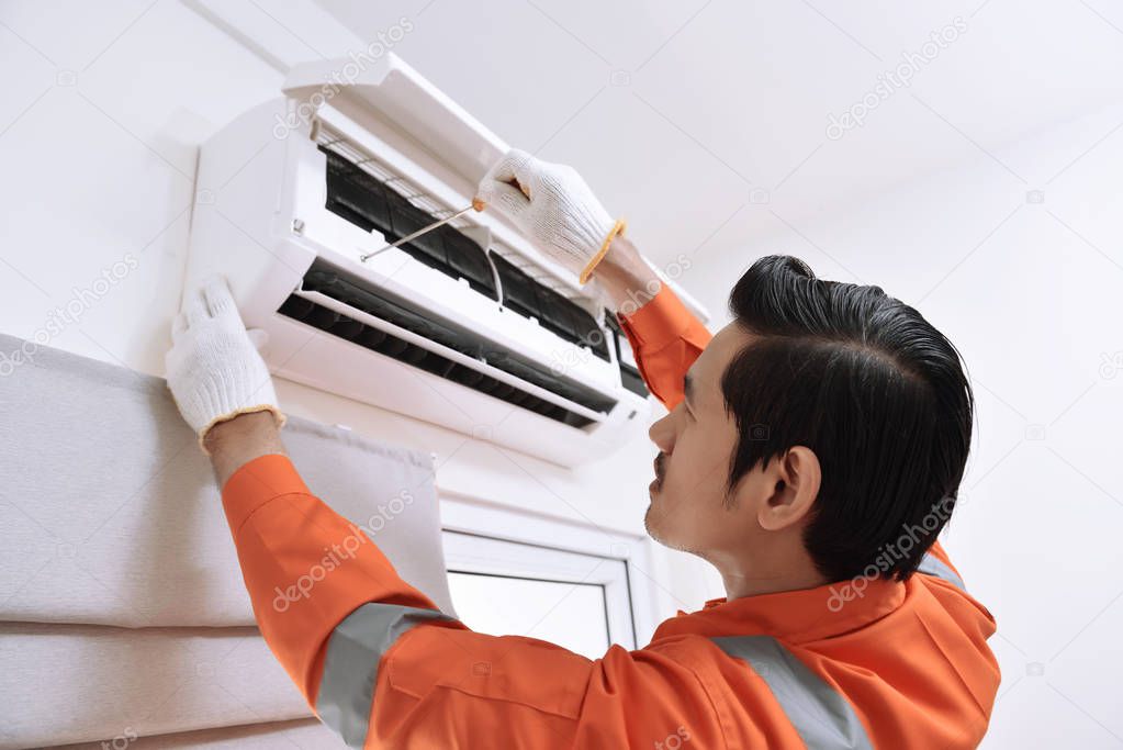 Young asian male technician repairing air conditioner with screw
