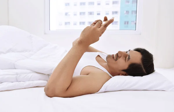 Hombre asiático acostado en la cama con teléfono inteligente — Foto de Stock