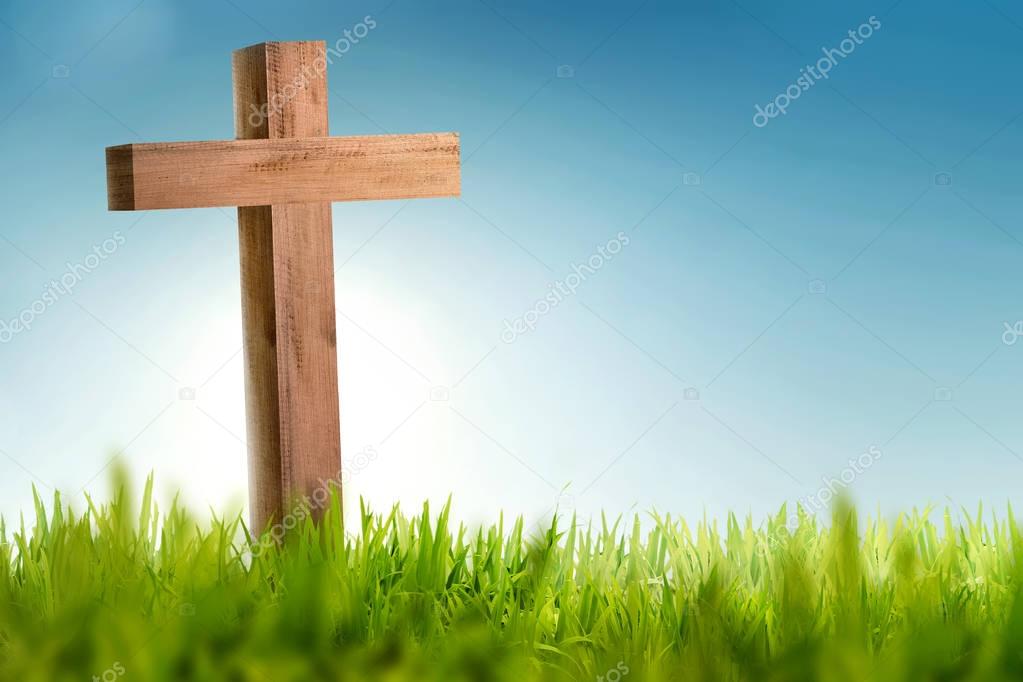 Wooden christian cross on green grass with blue sky background