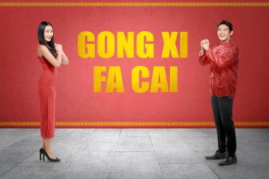 Mutlu Çin çift kırmızı duvar arka plan üzerinde Gong Xi Fa Cai metin ile cheogsam giysili. Mutlu Çin yeni yılı