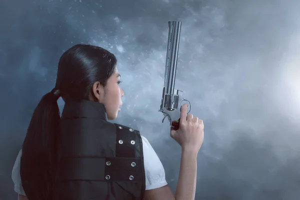 在黑暗背景下手持枪支的亚裔女子的背影 — 图库照片