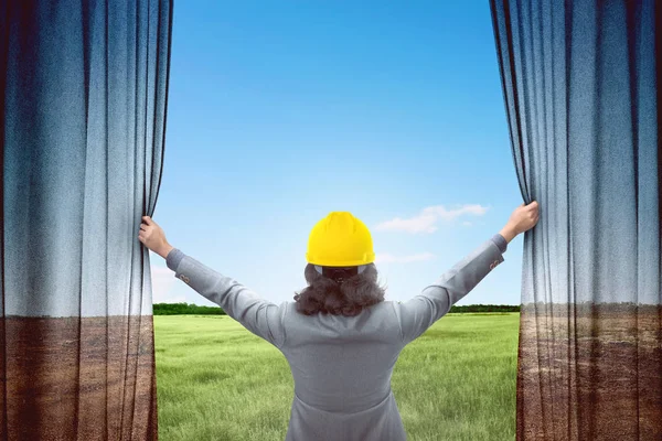 カーテンを開くと青い空を背景に緑の風景を見て魅力的な建築家の女性 — ストック写真