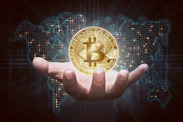 デジタル世界地図背景に仮想マネーとして黄金 Bitcoin を示す男性の手 ストックフォト