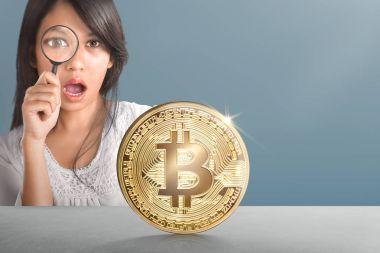 Young asian woman with magnifier looking at golden bitcoin on desk clipart