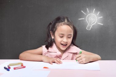 yeni fikir sahip olmak ve mum boya ile siyah arka plan üzerine çizim neşeli Asyalı küçük kız