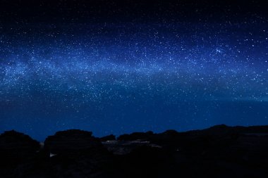 Parlak yıldızlı gece gökyüzü ile kayalık uçurum silüeti