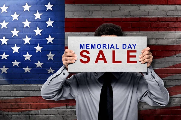 Businessman holding board with memorial day sale sign with american flag on background