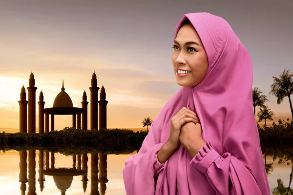 Young asian muslim woman with veil praying to god with mosque on background