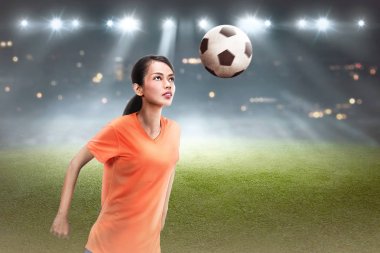 Genç Asyalı futbol oyuncu kadın başlığı topu alan üzerinde